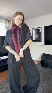 Crna oversized majica s kratkim rukavima, uparena s crnim širokim hlačama s kontrastnim šavovima, dopunjena maroon šalom.