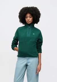 Grønn fleecegenser med kvart-glidelås, lange ermer og kengurulomme. Har en teksturert kropp og liten logo på brystet.