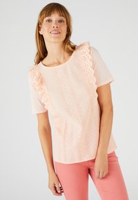 Top corto de manga corta en rosa claro con detalles de encaje y bordes en forma de ola, que presenta un patrón texturizado y un corte holgado. Combinado con pantalones rosas.