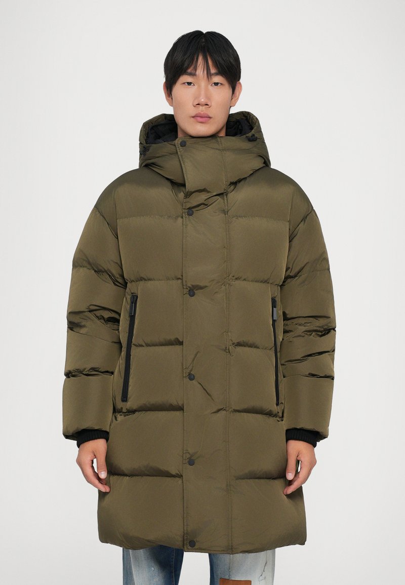 Giacca puffer verde oliva con cappuccio, caratterizzata da un design a righe orizzontali, bottoni a scatto e tasche laterali con zip. Materiale leggero.