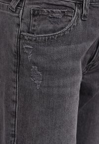 Jeans de denim negro para hombre con detalles desgastados, que cuentan con un diseño clásico de cinco bolsillos y costuras visibles sobre una tela texturizada.