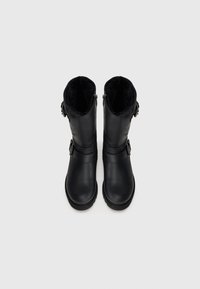 Botas pretas até à metade da panturrilha com fivelas nas laterais e interiores forrados a pelo, vistas de cima sobre um fundo branco.