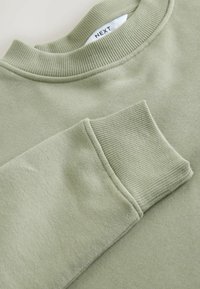 Gaiši zaļš džemperis ar ribotu apaļu apkakli un aprocēm. Mīksta tekstūra, ar gludu virsmu un izsmalcinātu šuvju apdari.