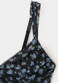 Soutien-gorge en résille noire avec motif floral bleu, bretelle ajustable et bordure en dentelle festonnée le long du bord supérieur.