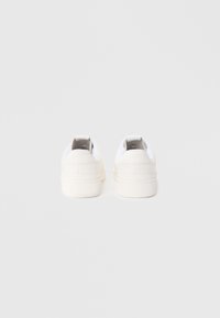 Baskets blanches avec une texture de tissu lisse, bout arrondi et design bas. Présente une doublure intérieure grise discrète et un onglet au talon.