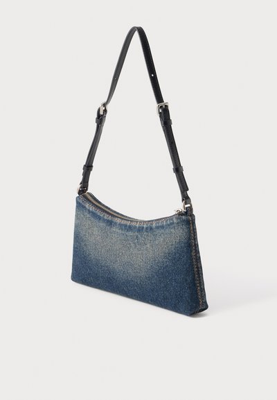 Petit sac à épaule rectangulaire en denim avec sangle noire réglable et fermeture éclair argentée sur le dessus, sur fond blanc.