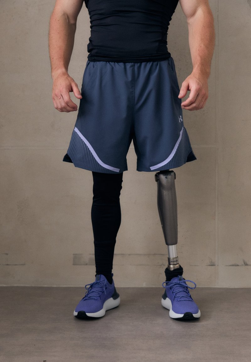 Idrottare bär svart åtsittande tröja, mörkgrå shorts med meshdetaljer och lila sneakers, och visar upp en metallprotes på höger ben.