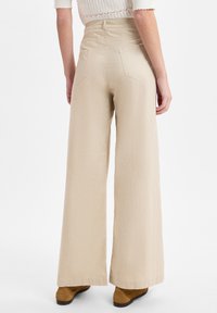 Beige wijde broek met een textuurstof, hoge taille en achterzakken, gecombineerd met bruine enkellaarzen.