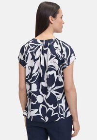 Marinebluse med hvidt blomsterprint, korte ærmer og rynket halsudskæring. Glat stof med en løs pasform, velegnet til afslappet brug.