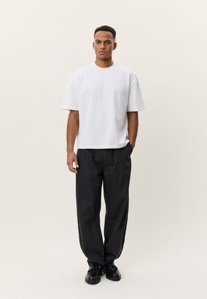 Άσπρο βαμβακερό μπλουζάκι με κοντά μανίκια, σε συνδυασμό με άνετο μαύρο παντελόνι και μαύρα παπούτσια, τοποθετημένα σε ουδέτερο φόντο.