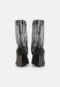 Botines negros con tacones de bloque, que presentan patrones abstractos en blanco y azul claro. Detalle de cremallera dorada en la parte trasera. Material de cuero suave.