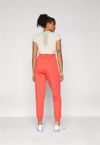 Lys beige cropped topp med utskjæring på baksiden, parret med lyse korall joggebukser og hvite joggesko med lilla detaljer. Glatt, tettsittende stoff.