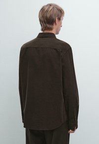 Dunkelbraunes Hemd mit Knöpfen, langen Ärmeln, Kragen und einer glatten, matten Textur. Verfügt über einen abgerundeten Saum und knöpfbare Manschetten.