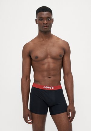 Schwarze Boxershorts mit einem roten Levi's Bund, aus weichem Baumwollmaterial und in figurnaher Passform. Das Model steht mit entspannten Armen an den Seiten.