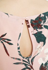 Blusa floreale rosa con un'apertura a chiave sulla schiena, fissata con un bottone abbinato. Motivi a foglia in verde e bordeaux decorano il tessuto.