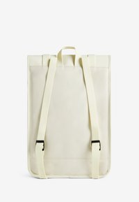 Un sac à dos en tissu crème doux avec une finition mate. Il dispose de deux bretelles ajustables, d'une poignée supérieure et de boucles noires pour la fermeture.