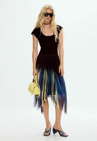 Must on lühikeste varrukatega must ülikond, plekitud seelik sinise, kollase ja musta gradatsiooniga, millele on lisatud kollane kott ja sinised kontsad.