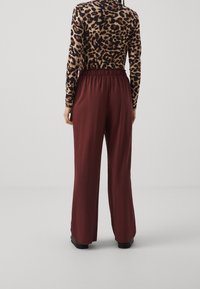 Bordeaux breda byxor med elastisk midja, i kombination med en långärmad topp med djurtryck som har en figurnära design och en slät yta.