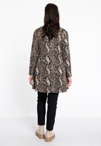 Langsleeve tuniek in een slangenprintpatroon, met tinten bruin en zwart, gecombineerd met slanke zwarte broek en beige enkellaarsjes.