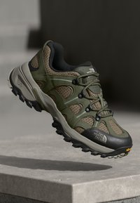 Zielone buty outdoorowe z siateczkowego i syntetycznego materiału, wytrzymała czarna gumowa podeszwa, system sznurowania zapewniający pewne trzymanie oraz logo marki z boku.