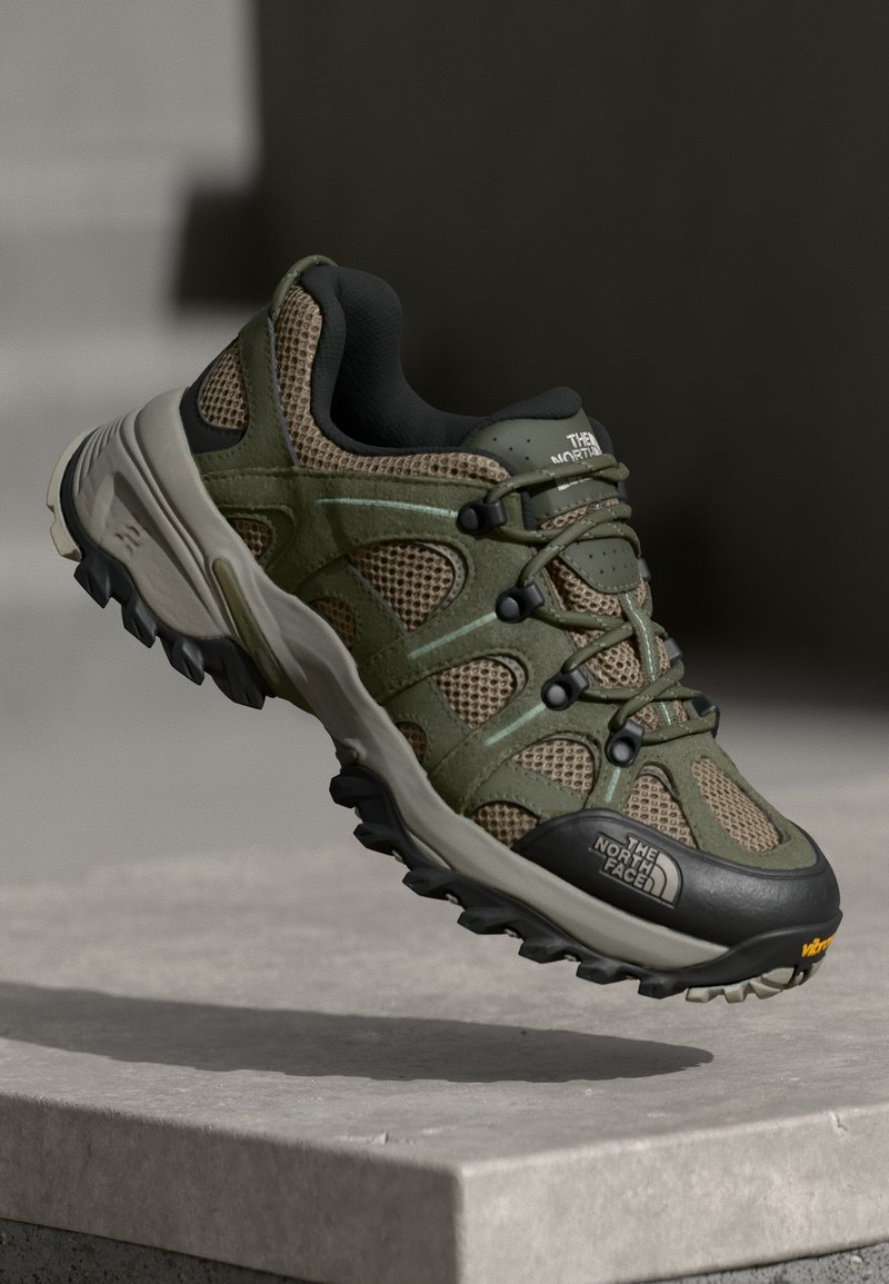 Zielone buty outdoorowe z siateczkowego i syntetycznego materiału, wytrzymała czarna gumowa podeszwa, system sznurowania zapewniający pewne trzymanie oraz logo marki z boku.