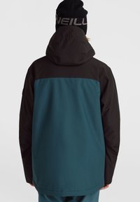 Chaqueta en azul verdoso y negro con capucha, que presenta un diseño elegante, una textura suave y un patrón horizontal en contraste en la parte trasera.