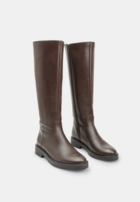 Botas de cuero marrón hasta la rodilla con un acabado suave, punta cuadrada, suela plana y cremallera lateral para facilitar su uso. Diseño y costuras minimalistas.