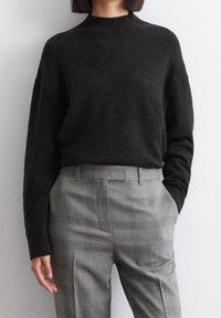 Pull en maille gris foncé avec un col montant, associé à un pantalon à carreaux gris clair, coupe ajustée et poches latérales.