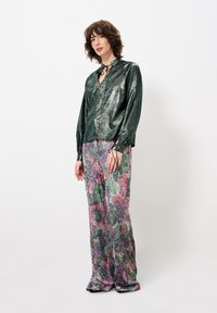 Glanzend groene langarmige shirt met een V-hals en strikdetail; gecombineerd met wijde broek in een kleurrijk bloemenpatroon.