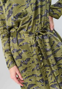 Grünes, gemustertes Kleid mit einem subtilen Tigerstreifenmuster in Grau und Gelb. Der Stoff hat eine glatte Textur und verfügt über eine taillierte Detail mit Knoten.