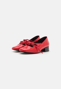 Red patent leather shoes with a pointed toe, low block heel, and crisscross laces. Features cutout designs on the sides.