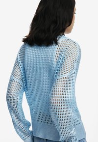 Hellblauer, transparenter Pullover mit strukturiertem, offener Strickmuster, langen Ärmeln und geripptem Saum. Hat eine lockere Passform mit sichtbarer Haut darunter.