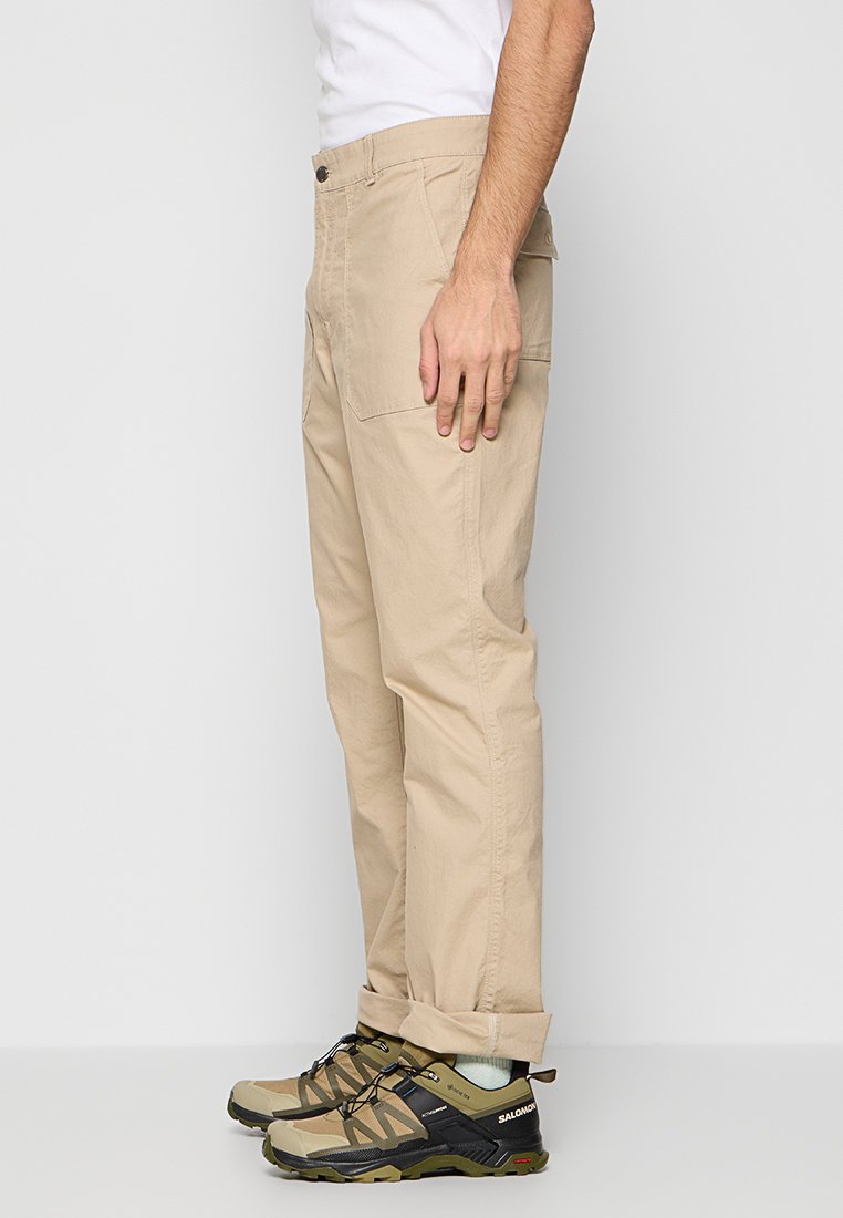 Pantalons cargo beiges, légers, avec de larges poches, coupe droite et ourlets retroussés, associés à des chaussures de randonnée robustes à lacets.