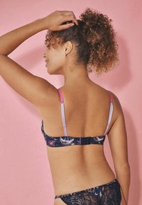 Trådløs bh i mørk navy stof med himmelske mønstre. Justerbare stropper i lys lavendel og pink. Blondekanter forneden.