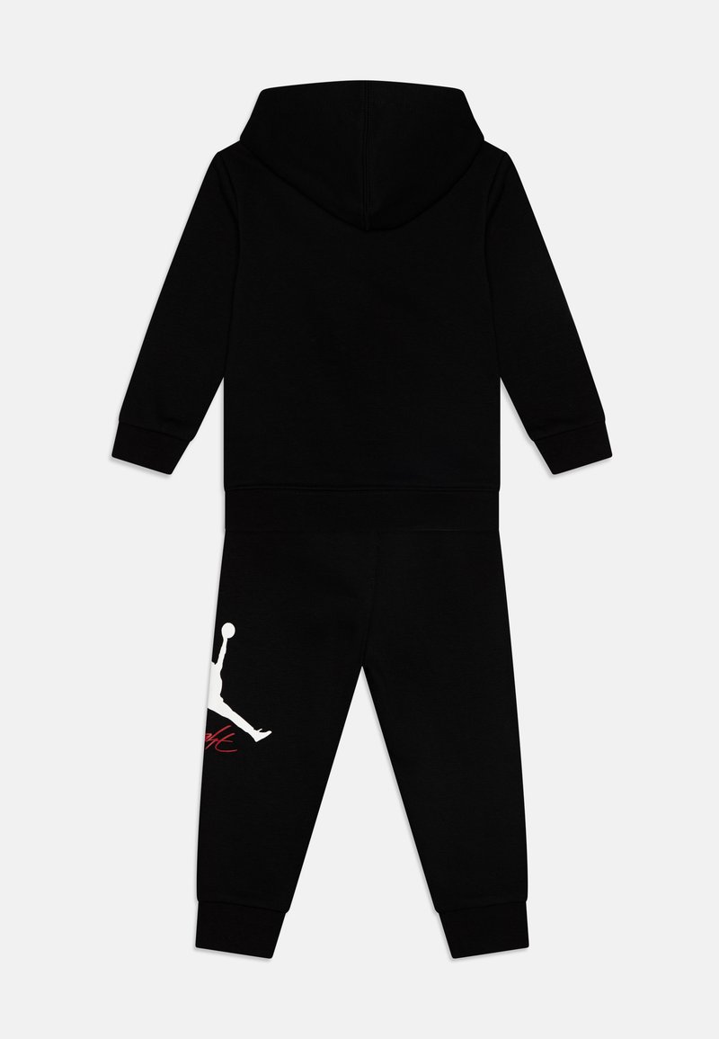 Sweat-shirt à capuche noir avec un pantalon assorti, doté de poignets élastiques et d'un grand logo Jumpman blanc sur la jambe gauche avec des accents rouges.