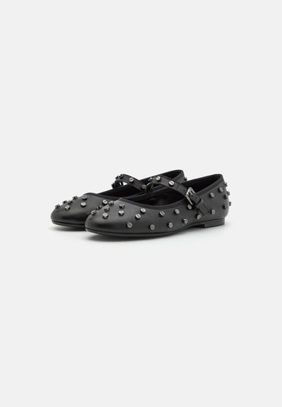 Ballerines en cuir noir avec une sangle réglable, ornées de clous en argent sur le haut et d'un bout arrondi. Texture lisse, talon bas.