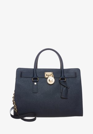 Bolso de cuero azul marino con dos asas, cierre dorado y colgante, y una correa de hombro desmontable con detalles de cadena.