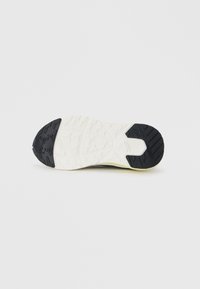 Semelle d'une sneaker avec une base blanche et des grips en caoutchouc noir au talon et à l'orteil, montrant un motif de semelle détaillé sur un fond uni.