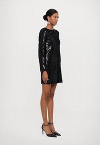Abito nero con paillettes, maniche lunghe e scollatura rotonda, di lunghezza al ginocchio, abbinato a décolleté nere con punta a mango e orecchini statement.