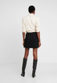 Pull en maille crème avec un col haut, associé à une mini-jupe noire texturée. Des bottes noires montantes complètent la tenue.