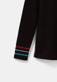 Czarna koszula z długim rękawem z żywym czerwonym i turkusowym geometrycznym haftem wzdłuż mankietu. Miękka tkanina o luźnym kroju.