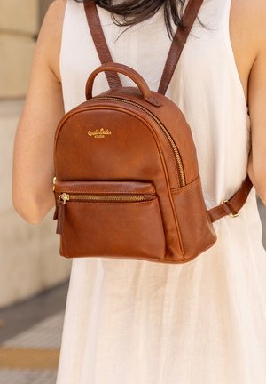 Brązowy plecak ze skóry kasztanowej z zaokrąglonym wierzchem, złotymi detalami, przednią kieszenią na zamek i regulowanymi ramiączkami. Gładka tekstura i subtelne logo.