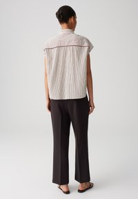 Top ampio a righe in crema e marrone scuro, con colletto alto e maniche corte, abbinato a pantaloni scuri a gamba larga.