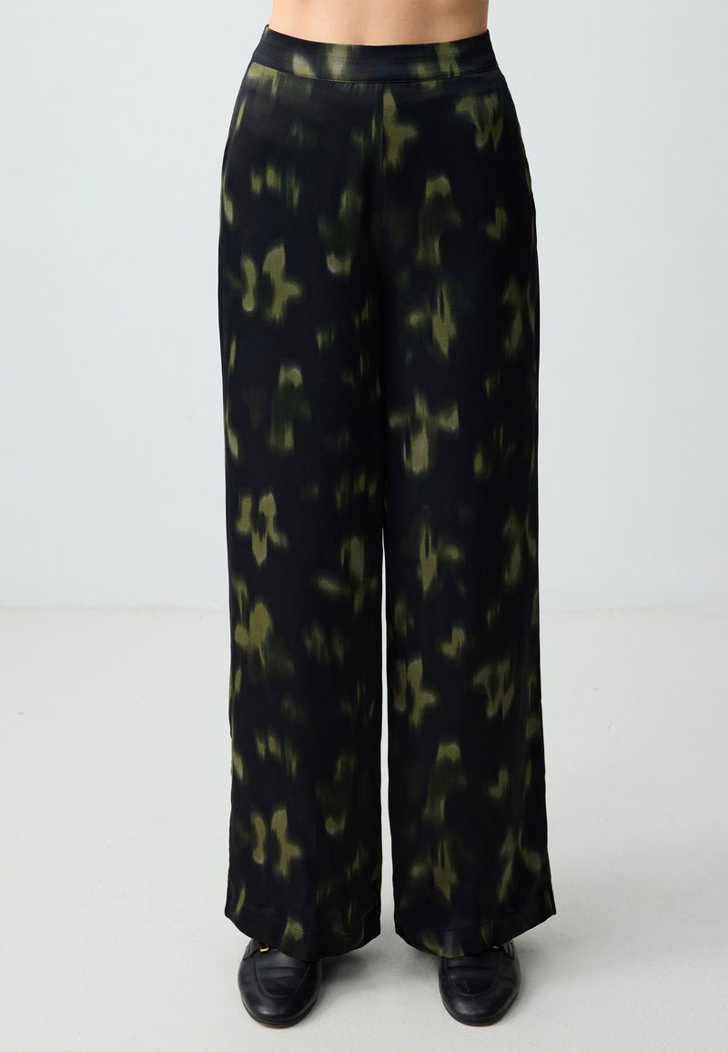 Zwarte wijde broek van stof met een groen abstract patroon. Glad textuur, elastische tailleband en volle lengte.