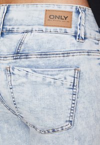 Izblijedjeli svijetloplavi traper hlače s kožnom etiketom branda "ONLY." Imaju stražnje džepove i vidljive detalje šivanja.
