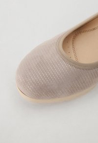 Light beige flat shoe with a soft, textured fabric upper featuring a subtle pattern, elasticized opening, and a light-colored rubber sole.