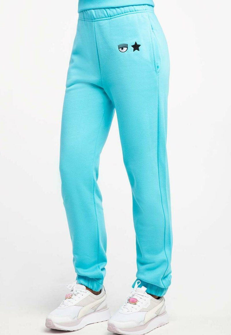 Hellblaue Jogginghosen mit einem elastischen Bund, seitlichen Taschen und schwarzen Augen- und Stern-Grafiken. Kombiniert mit weißen Sneakers mit rosa Akzenten.