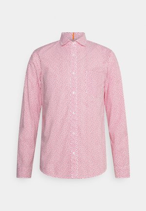 Biała długa koszula zapinana na guziki z czerwonym abstrakcyjnym wzorem kropek, kołnierzykiem w szpic i kieszenią na piersi z przodu.