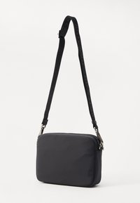 Sac bandoulière en nylon noir de forme rectangulaire, avec des accessoires en argent et une bandoulière ajustable à motifs. Texture lisse avec une fermeture éclair.