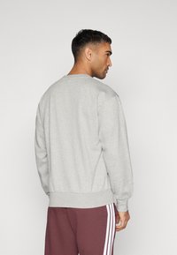 Sweatshirt cinza de gola redonda com mangas longas, punhos e bainha canelados. Textura de tecido suave, corte descontraído e design minimalista.